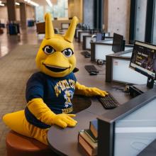 Sammy Slug mascot at a computer on campus