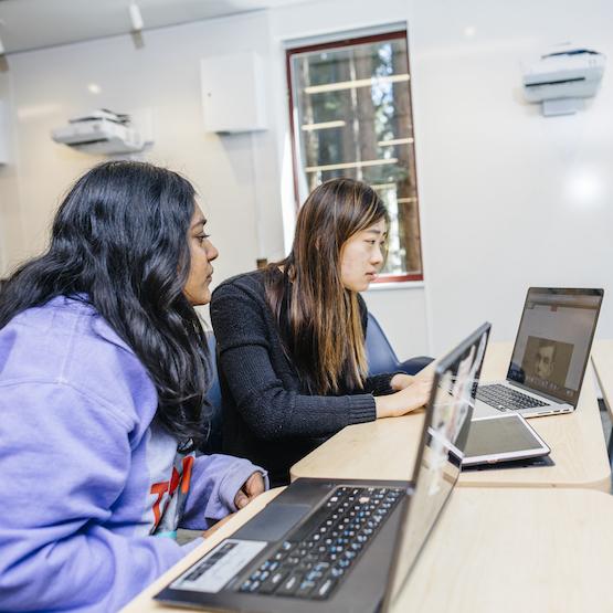 two female presenting students looking at laptops