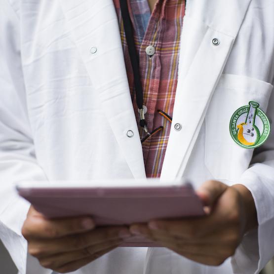 Student in white coat with tablet and "Green Labs" badge
