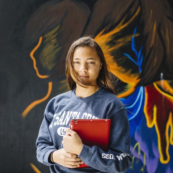 Student holding book in front of a mural