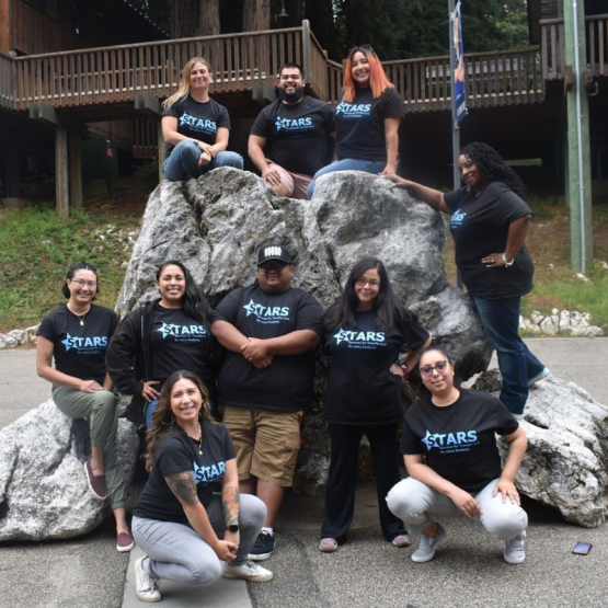 Group of STARS team members wearing black T-shirts posing around a large rock outdoors