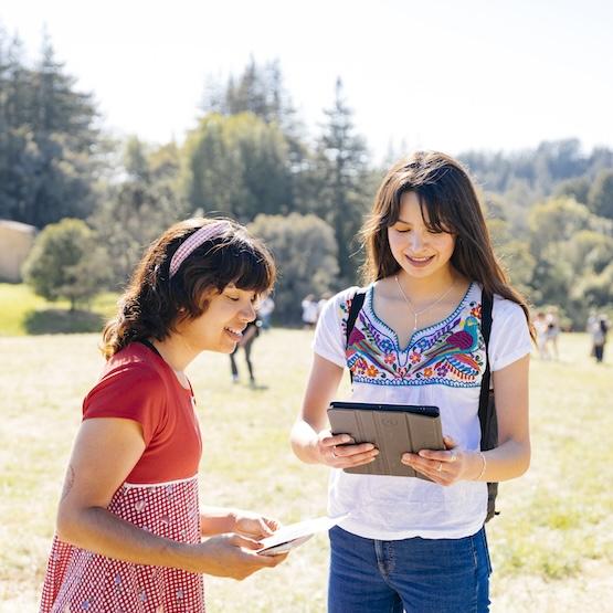 Two students standing outside looking at a tablet