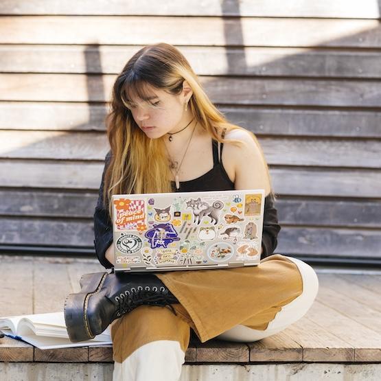 Student on a laptop outside, referring to a book